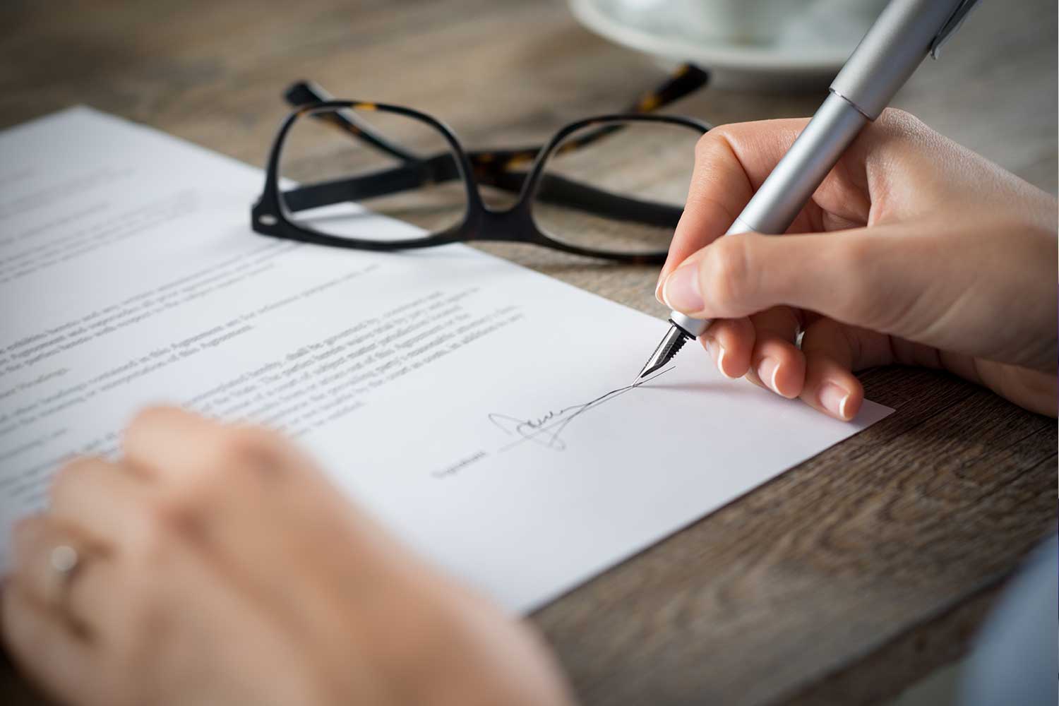close-up of a person signing a form with glasses on table