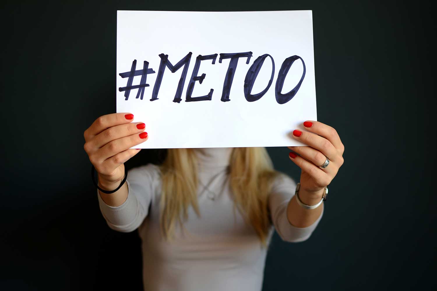 A young woman hold up a sign with "#METOO" emblazoned on it.