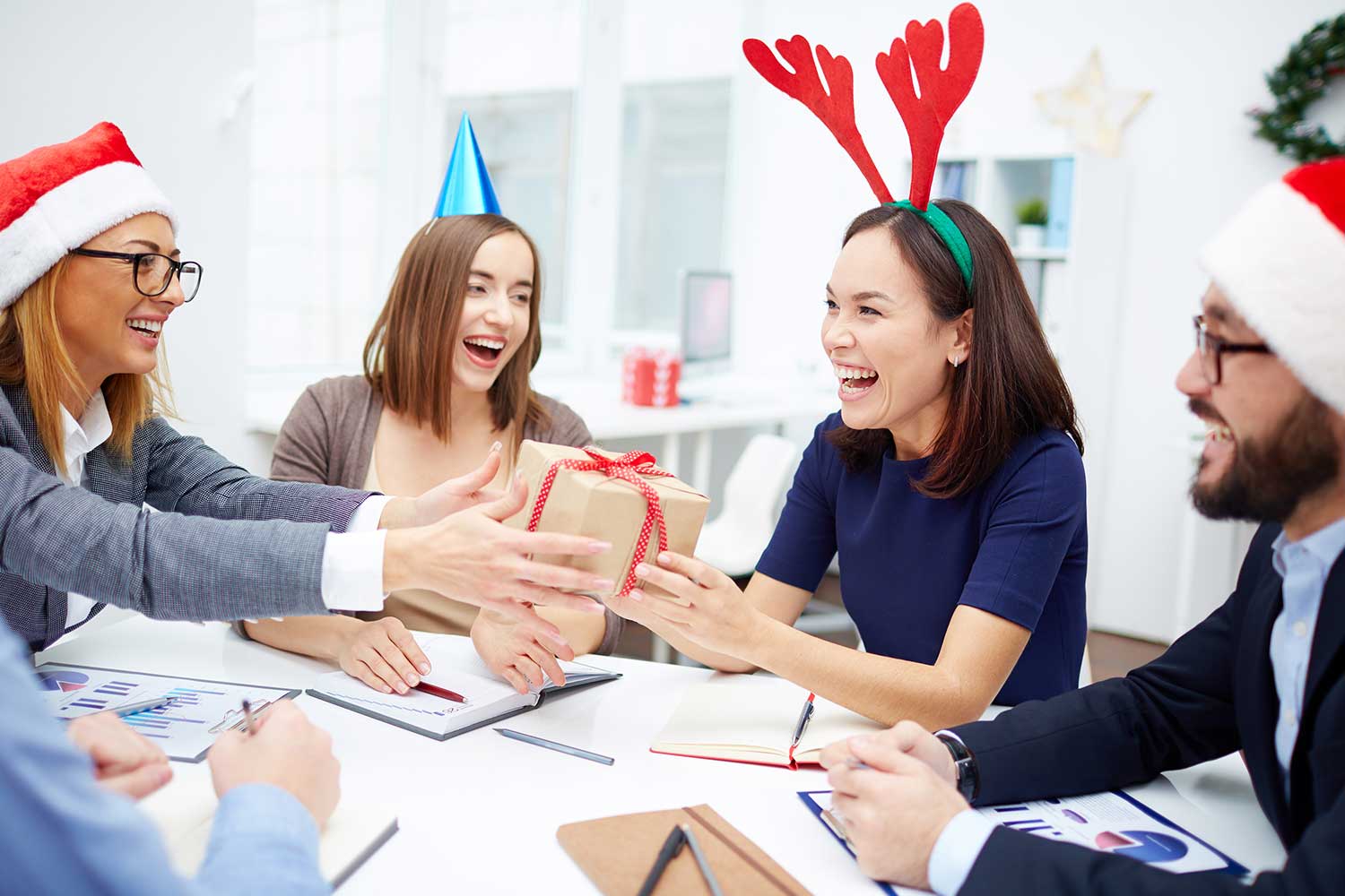 Four people wearing holiday headgear sit around a conference table.