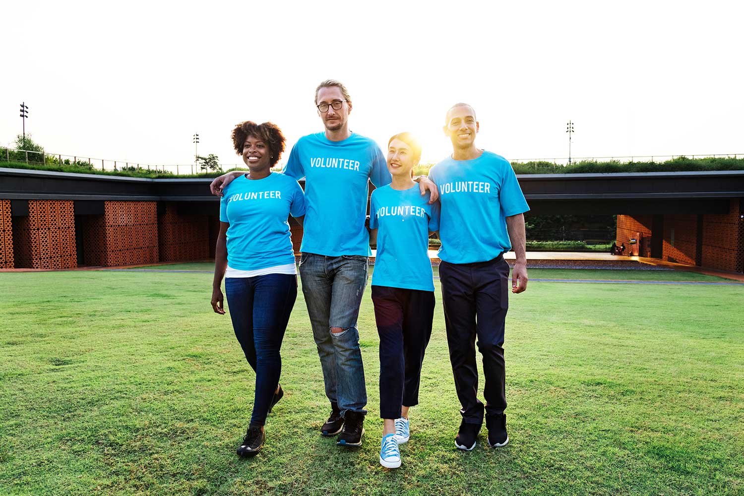Four people in blue shirts stand on a field.