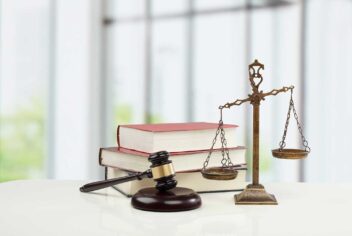 A judge's gavel is seen in front of some thick books and next to a justice scale.