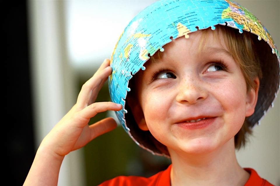 young smiling boy holding a globe puzzle on his head