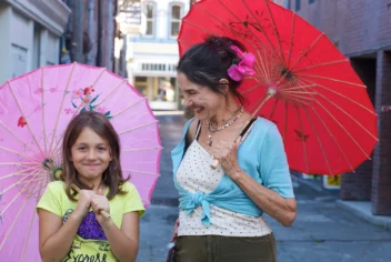 A woman and young girl have colorful parasols during the daytime.