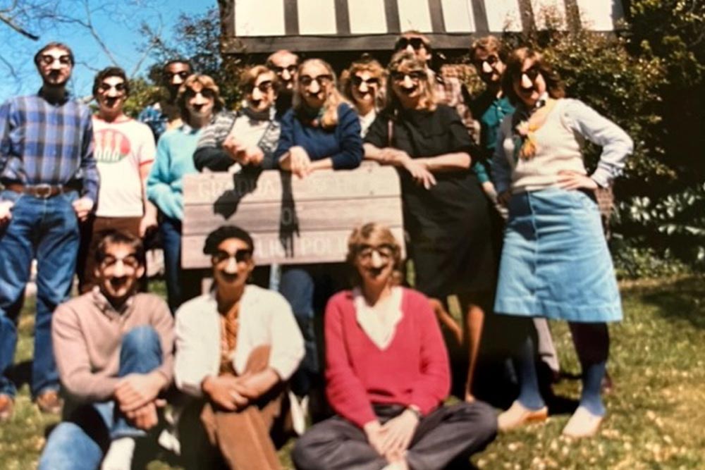 Aged photo of a bunch of students wearing Groucho Marx glasses, standing around a sign
