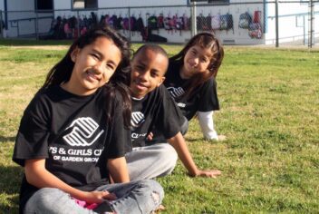 2 girls and 1 boy with Boys and Girls Club shirts sit on the grass