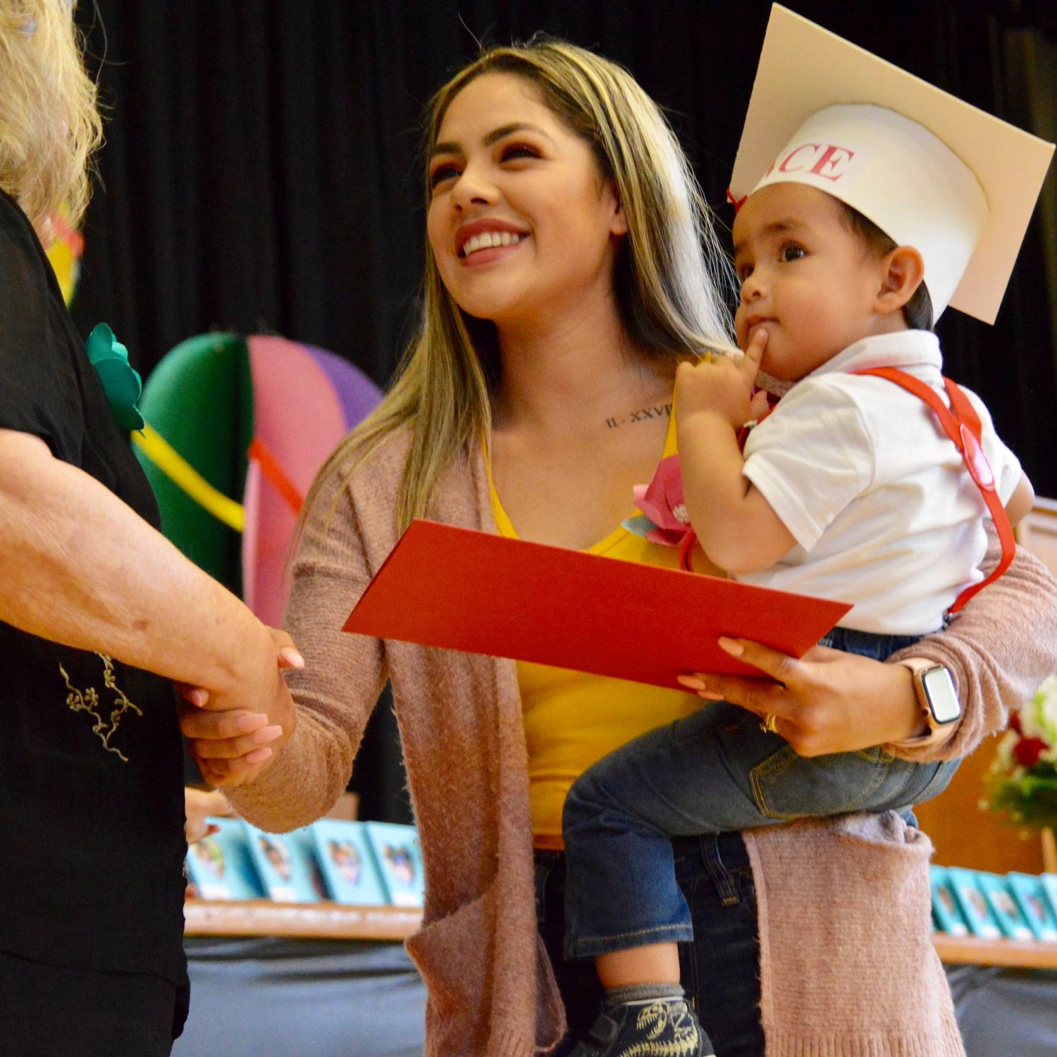 A young mother holding her toddler son while receiving a diploma