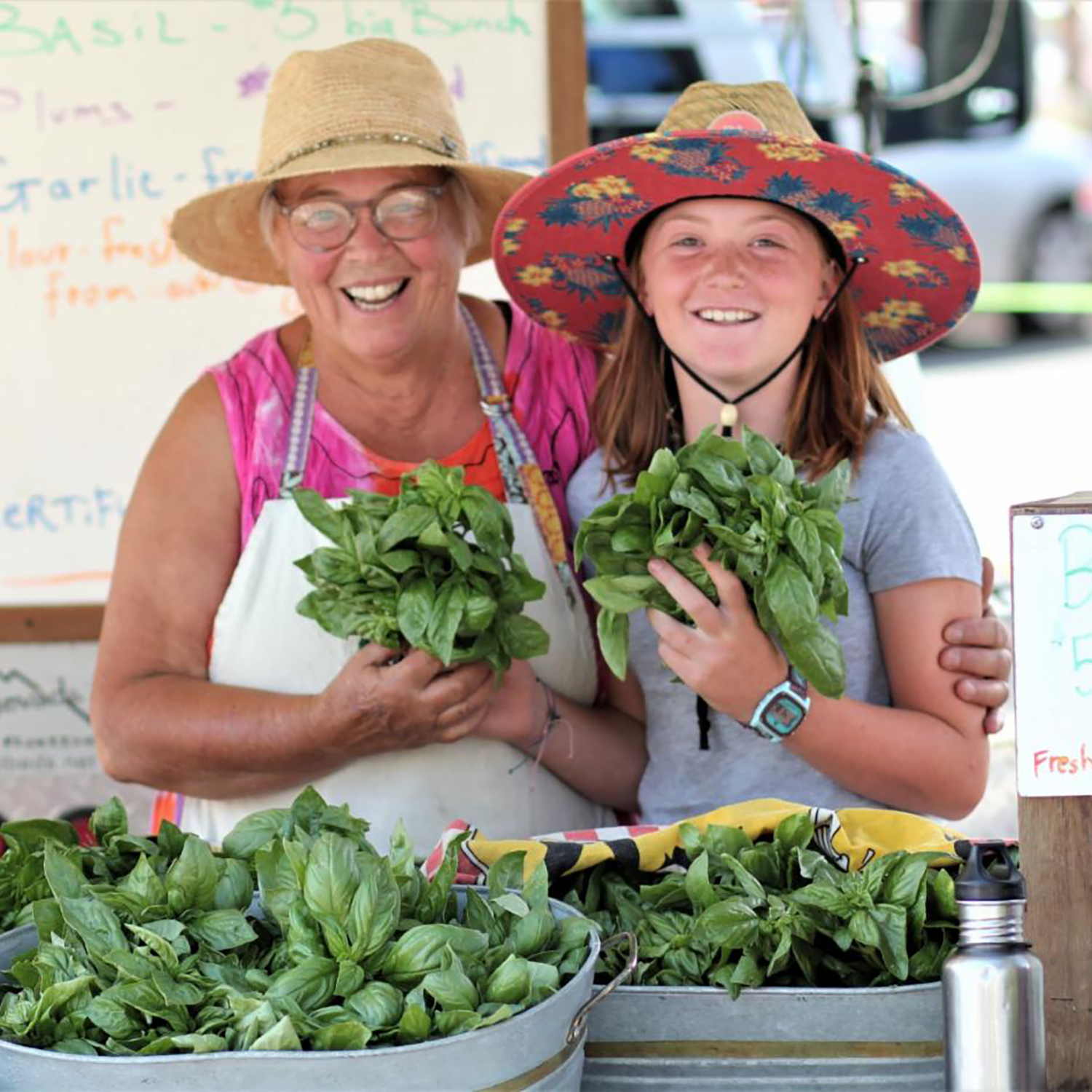 Two people in hats holding veggies at a farmer's market