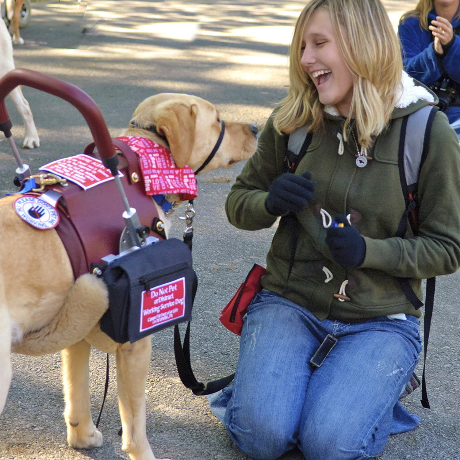 A smiling young woman kneels next to a service dog