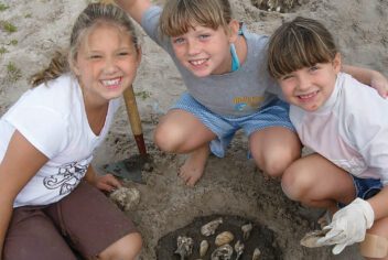 Three girls pose with seashells as they play in the sand