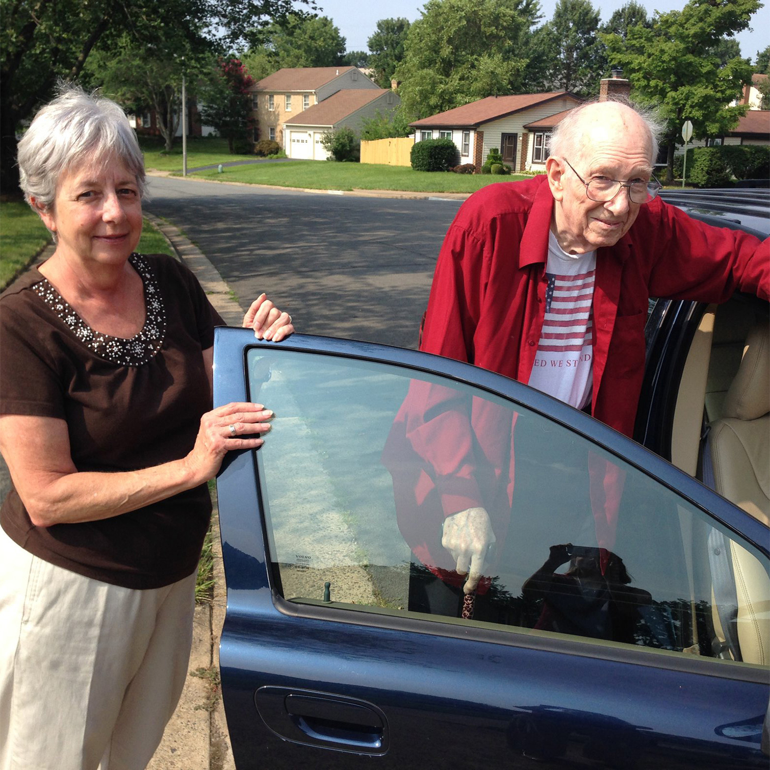 A woman holds a car door open for a senior man.