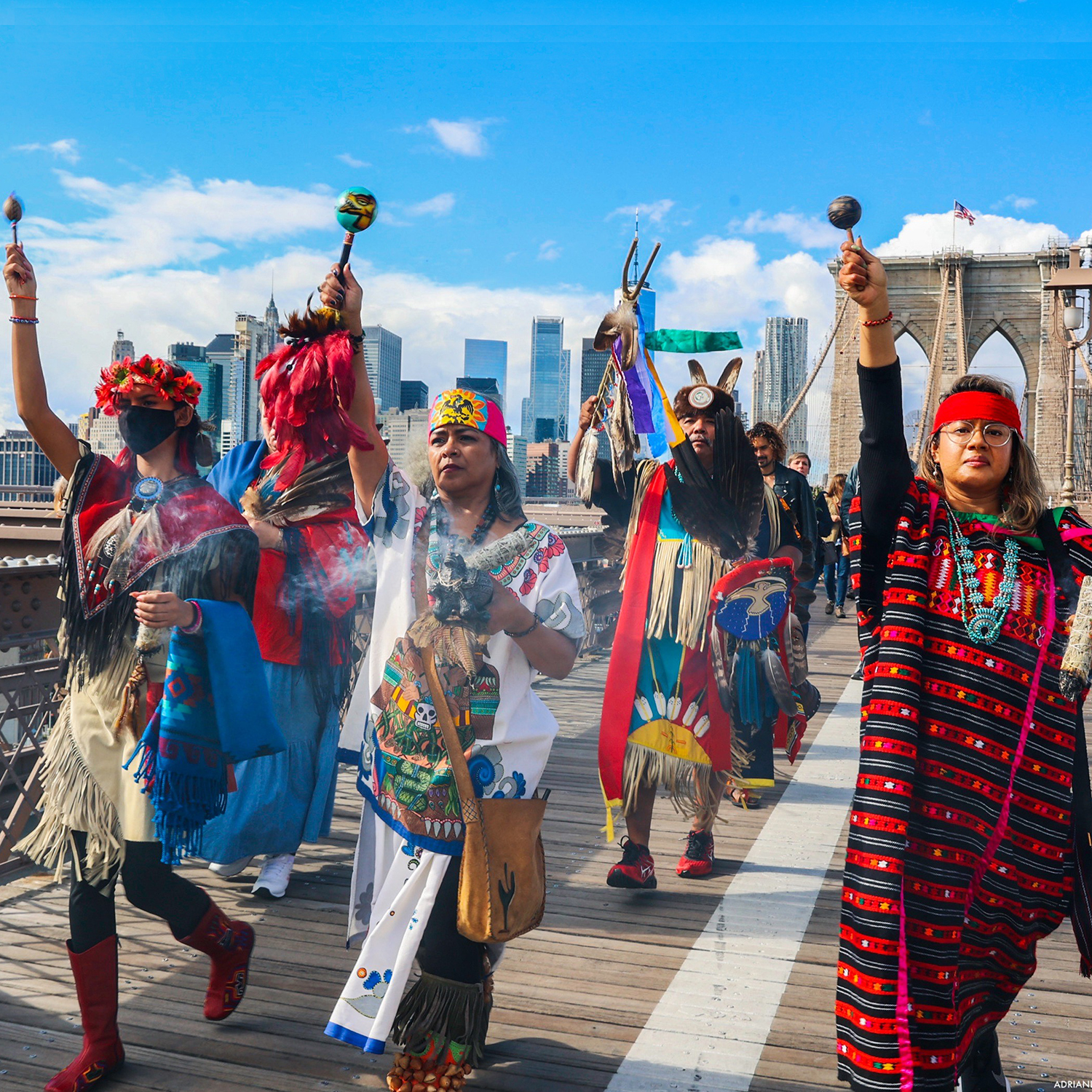 A group of people in native attire march across a bridge in New York