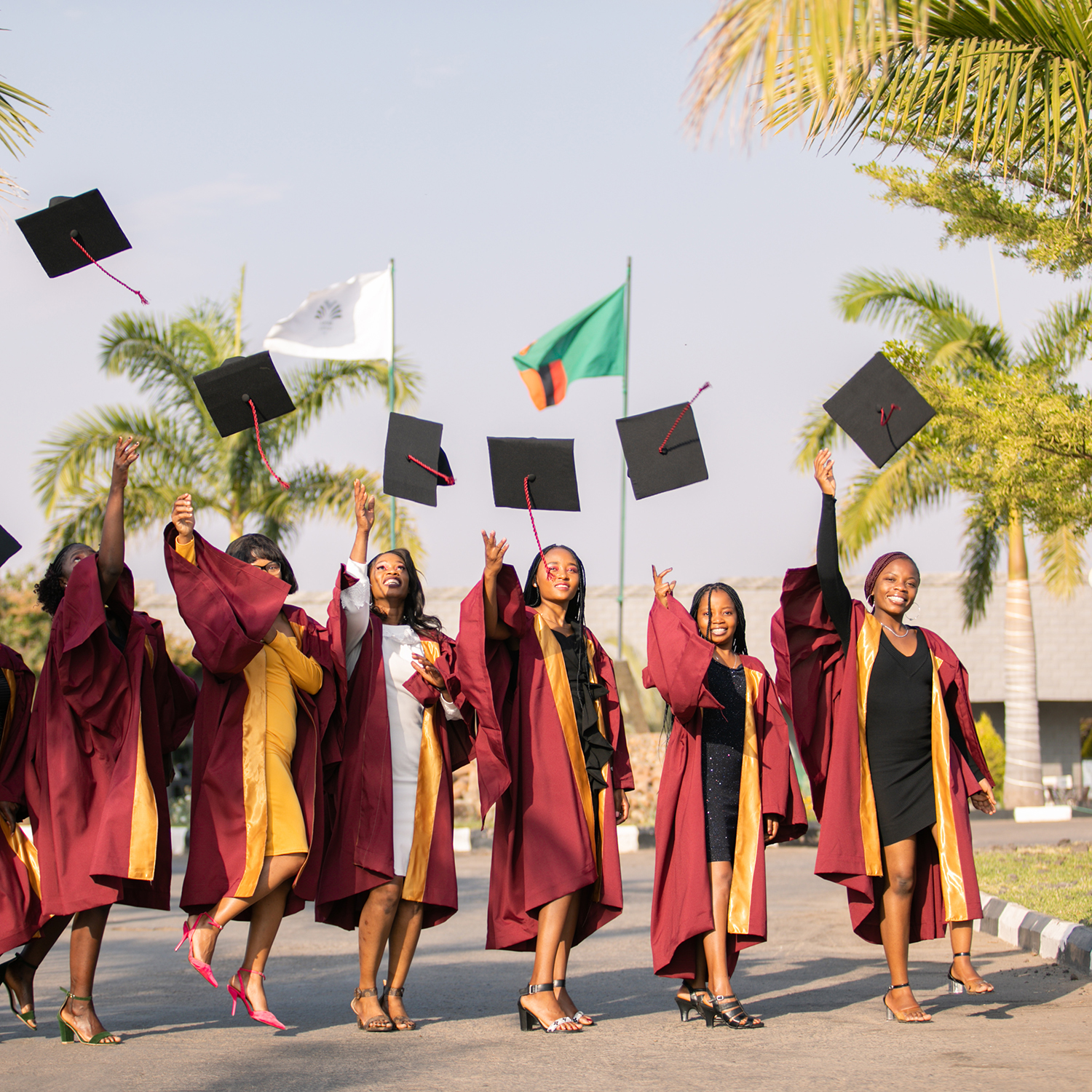 A group of young women in graduation gowns toss their caps in the air in celebration