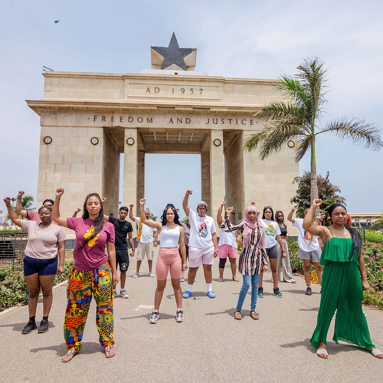 A diverse group of women stand with arms raised in front of a "Freedom and Justice" archway.