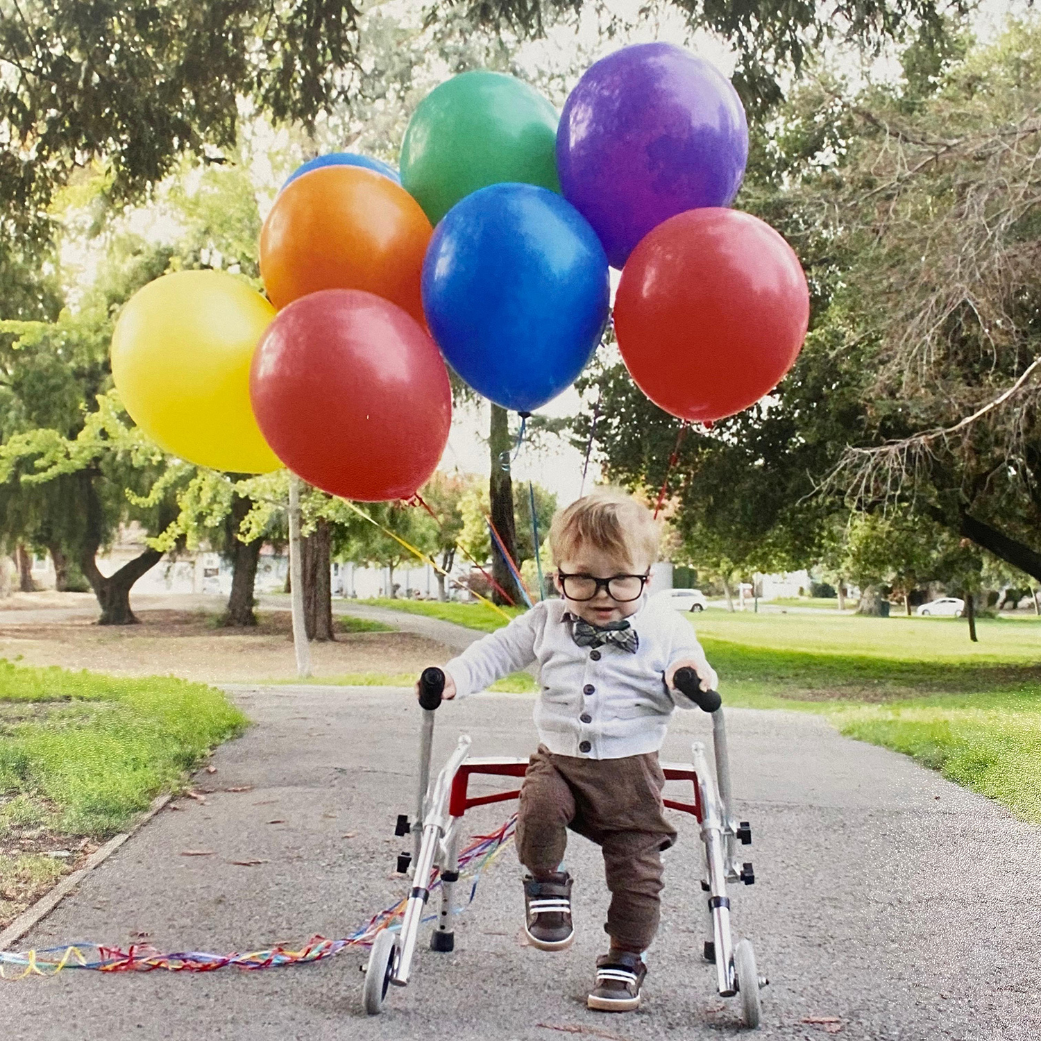 A boy using a walker carries a bunch of balloons
