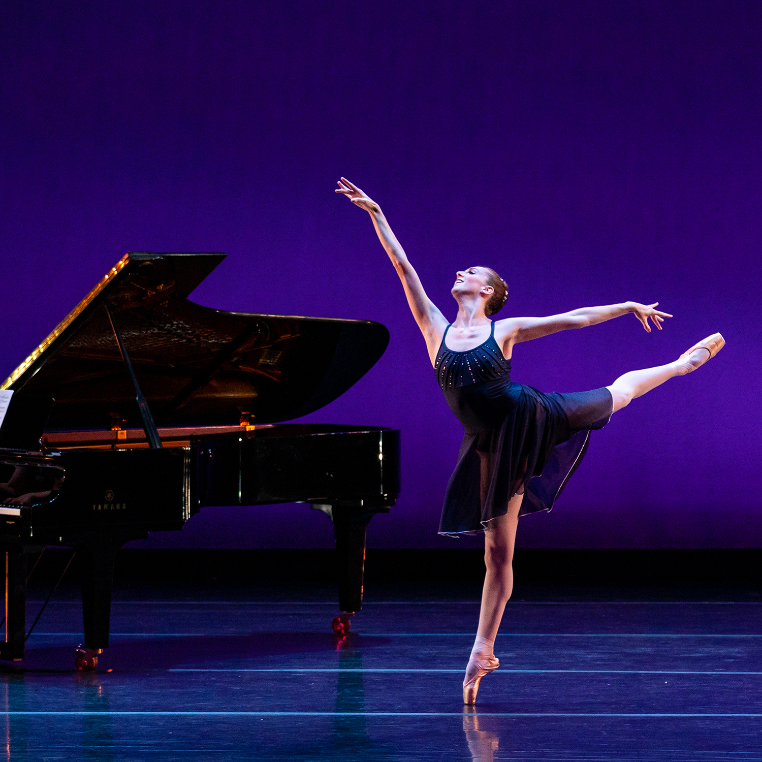 A ballerina dances near a grand piano on stage