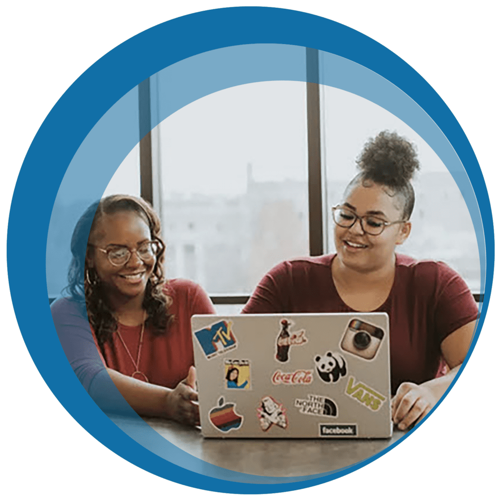 two young women look at a laptop together