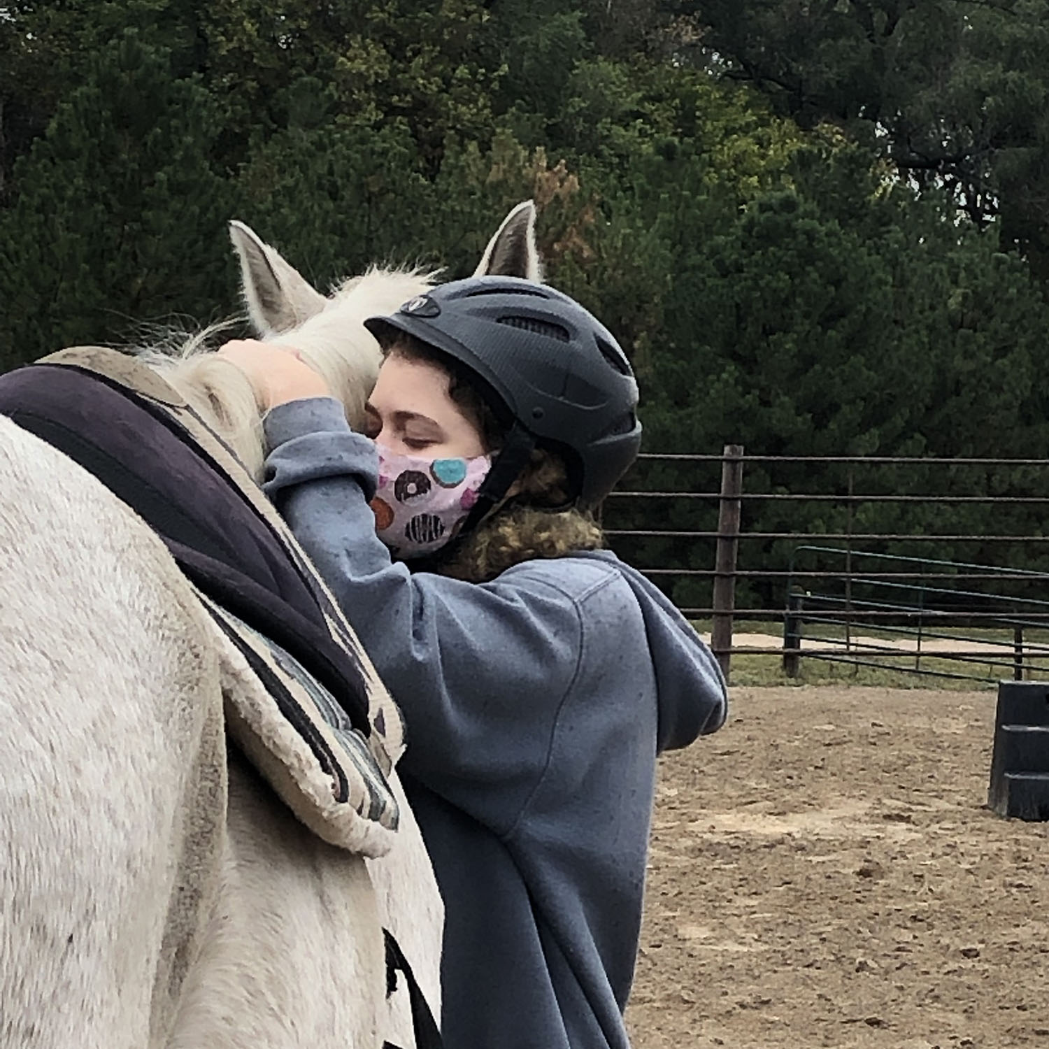 a teenage girl wearing a mask hugs a white horse