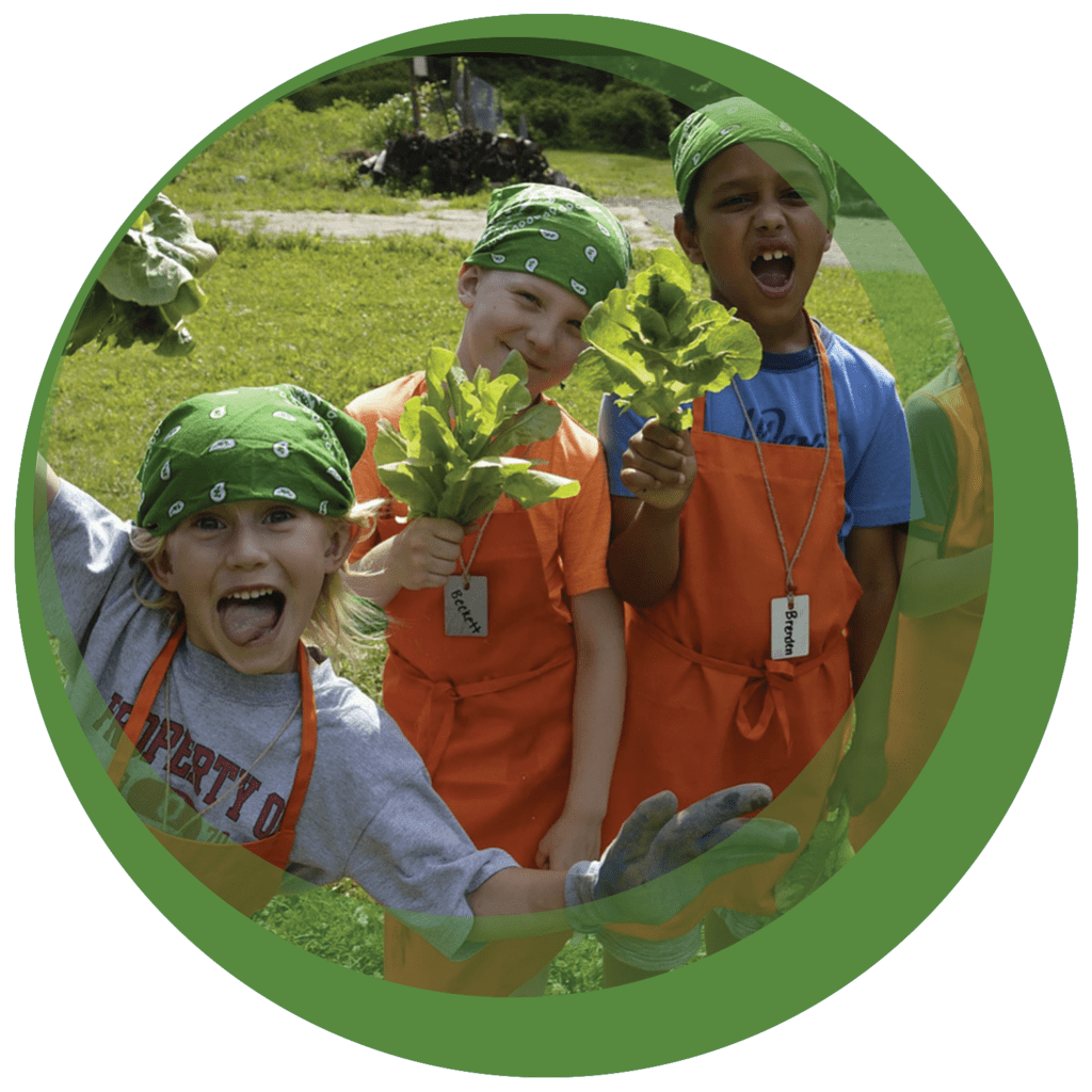 three children in aprons and bandana hold lettuce they picked outside