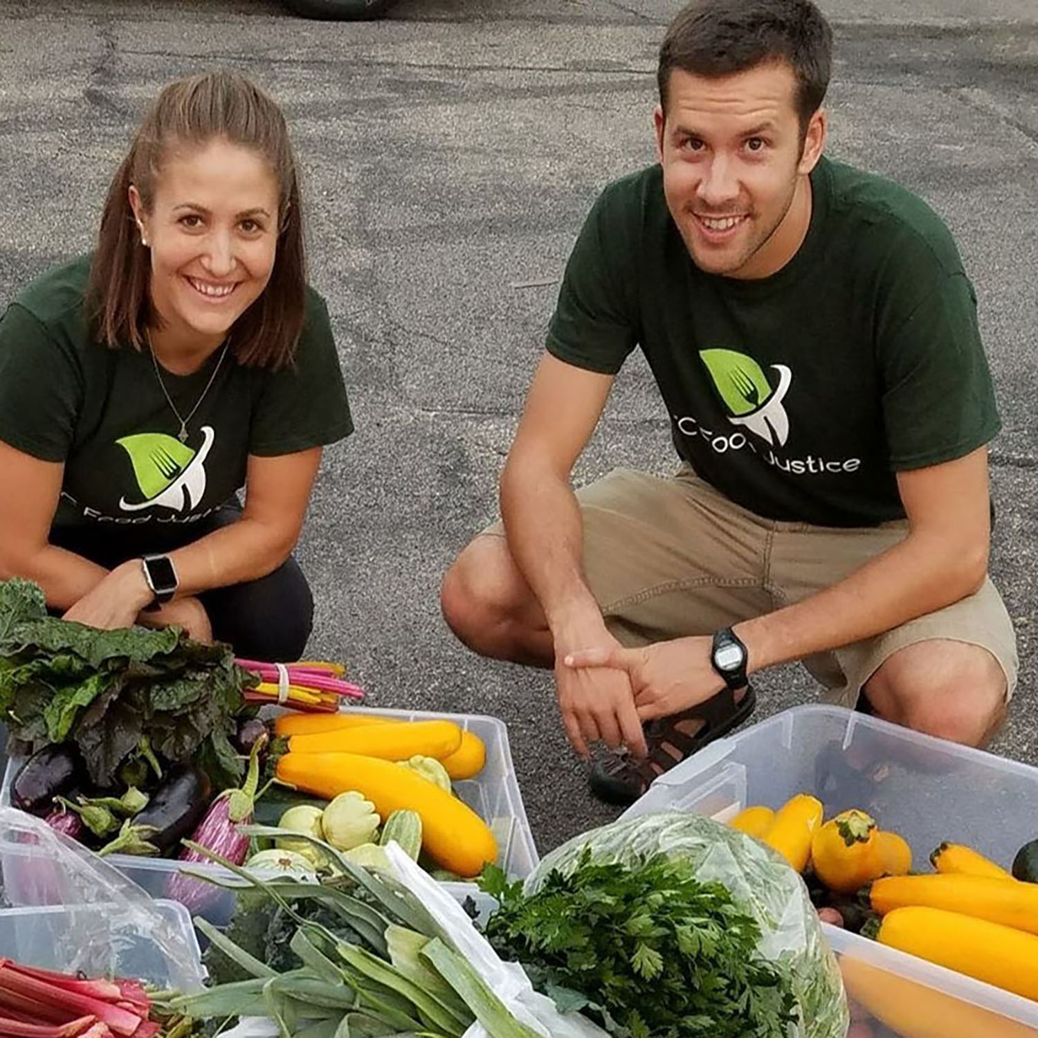 two people smiling behind large containers of produce