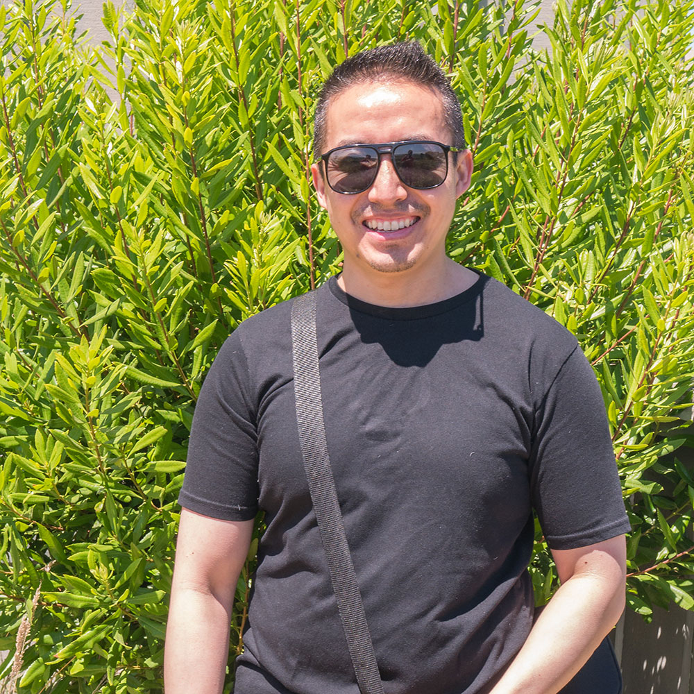Navin L. standing in front of a bush wearing sunglasses