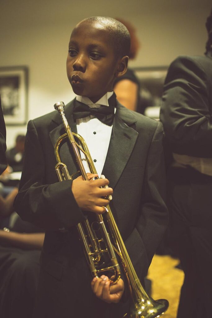 a boy in a tuxedo whistles while holding a trombone