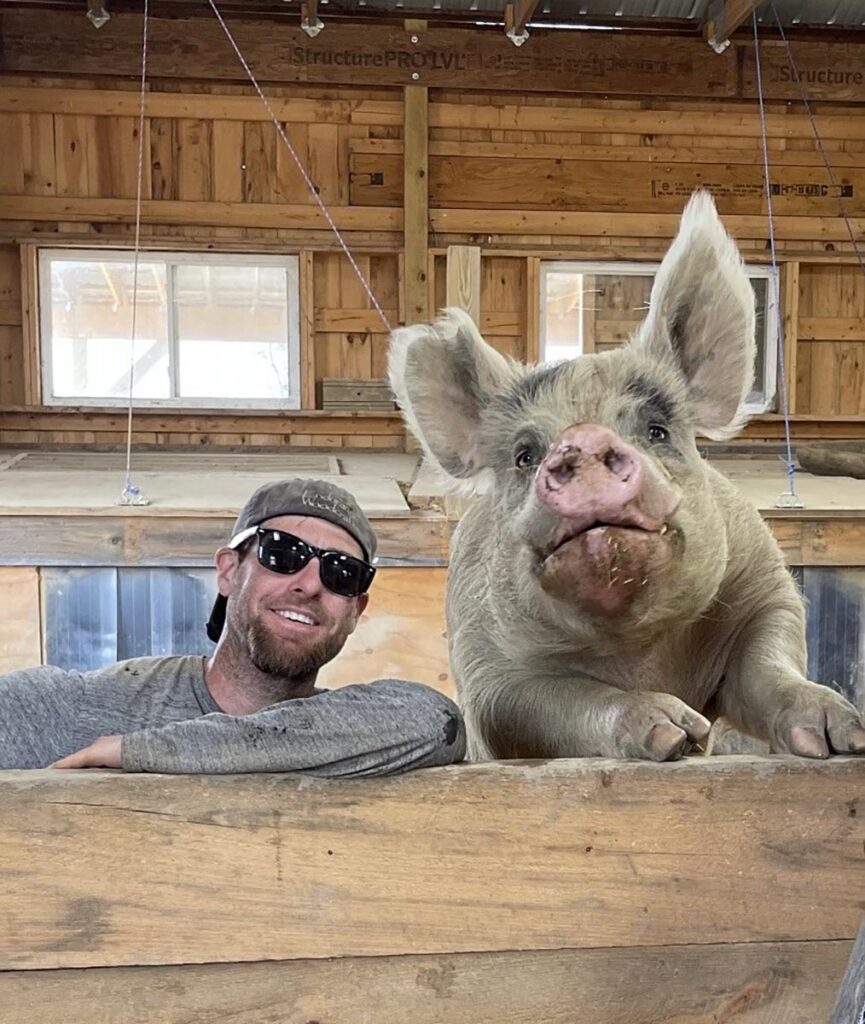 a man and a giant pig pose for the camera in a wood structure