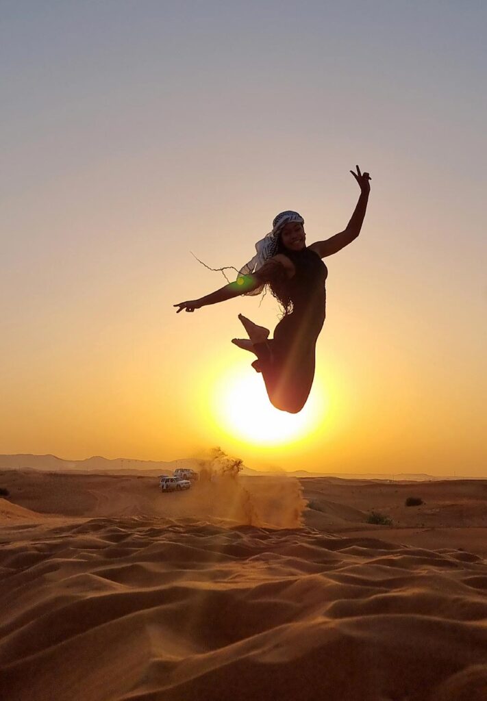 a woman jumps high above some sand dunes