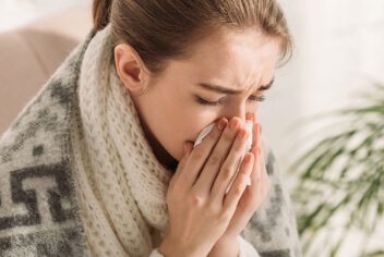 a woman wrapped in a blanket holds a tissue to her nose