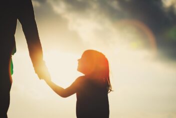 Silhouette of child holding parent hand at sunset