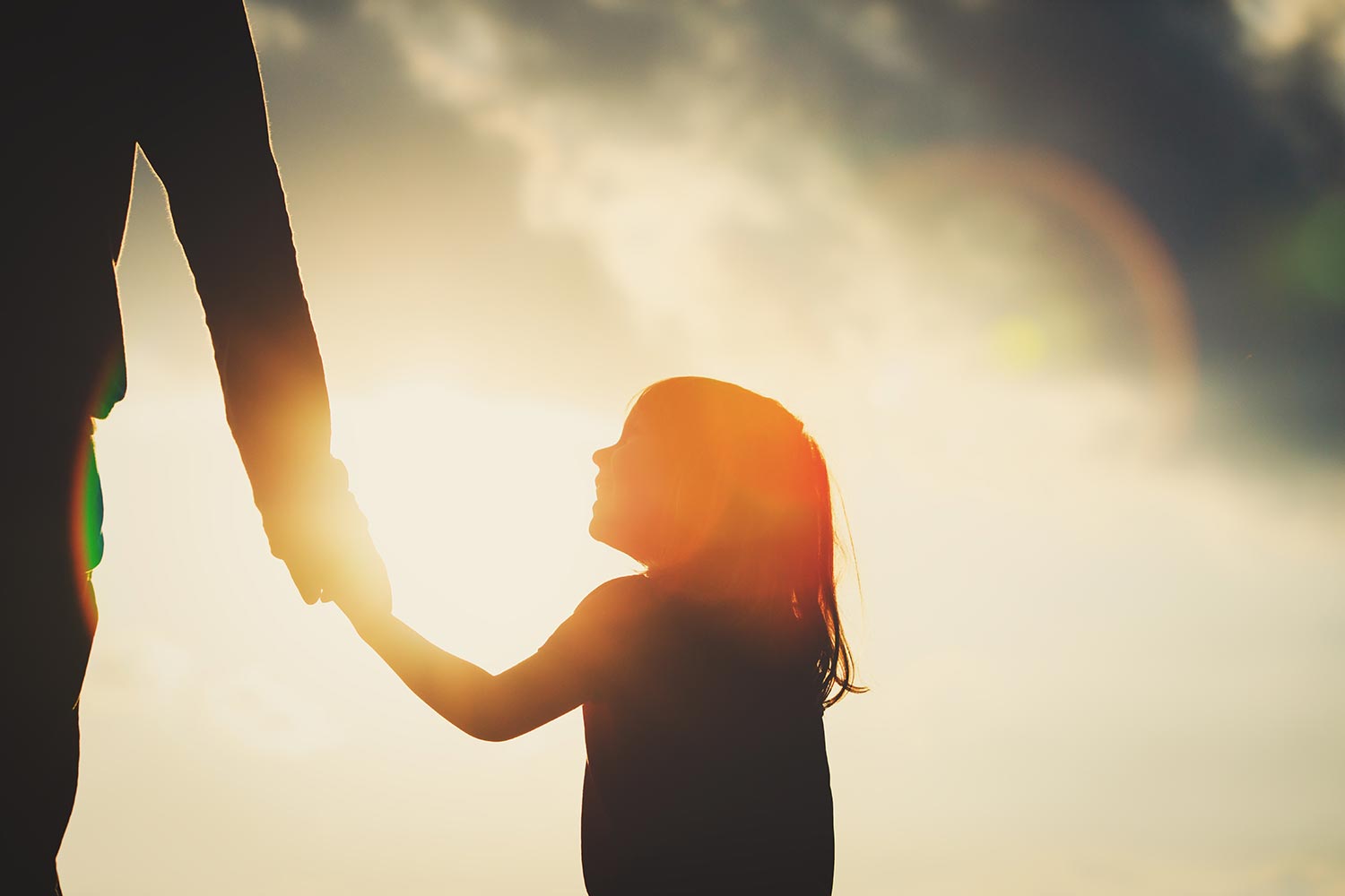 Silhouette of child holding parent hand at sunset