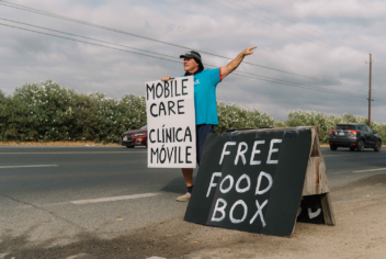 A person standing on the side of a road next to a sign that says "Free food box"