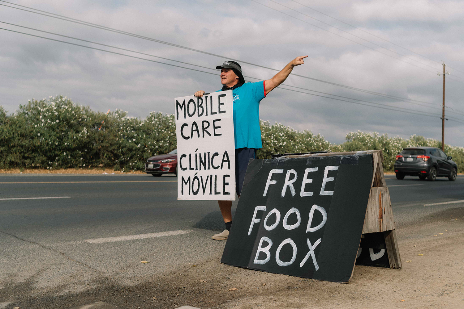 A person standing on the side of a road next to a sign that says "Free food box"