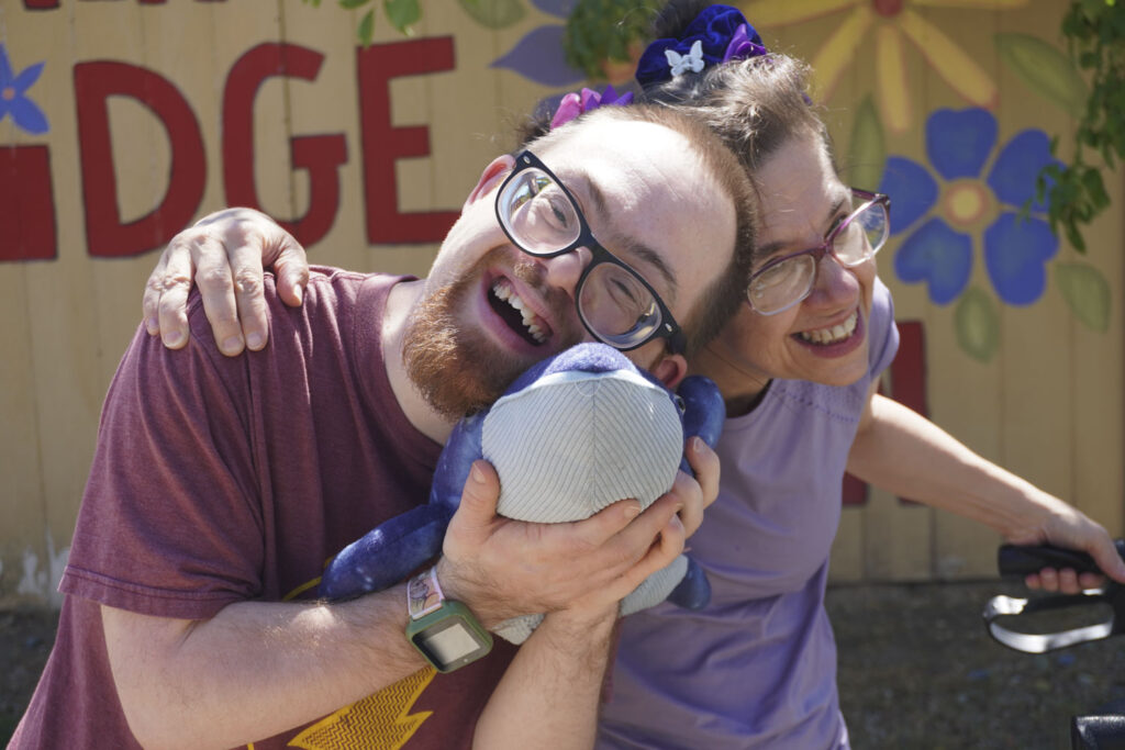 two people smile and hug a stuffed animal