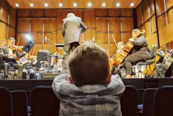 a small child viewed from behind watches a symphony perform