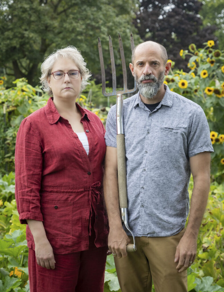 two people pose in a garden with a pitchfork