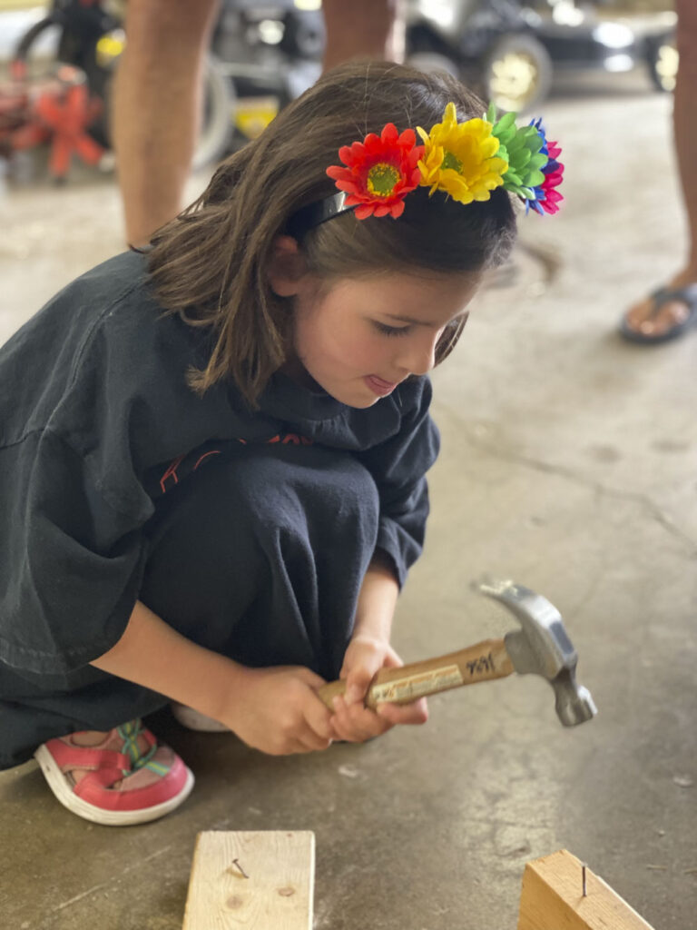 a child with a hammer squats to hit a nail