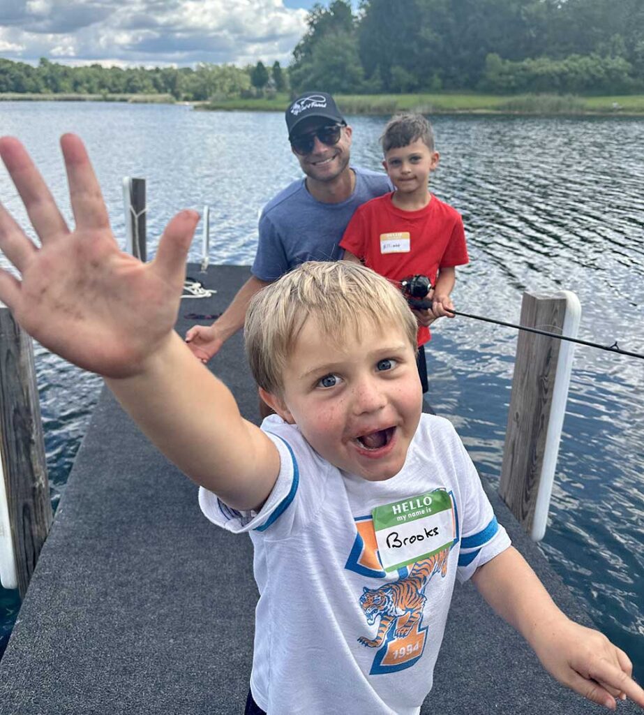 a young boy on a doc waves with two people fishing