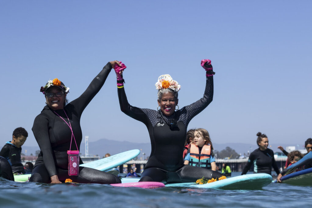 two people with arms raised while sitting on surfboards in a group