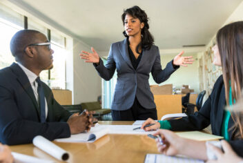 three people talk around a table with business papers