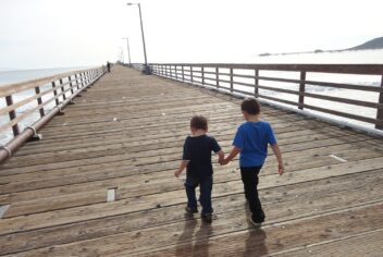 two boys walking hand in hand on a pier