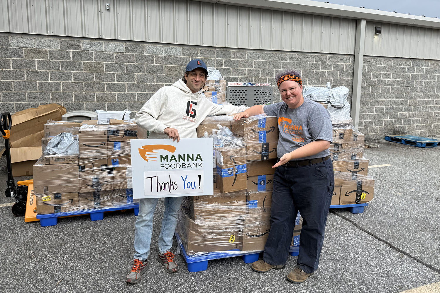 two people standing in front of pallets of boxes with a "thank you" sign