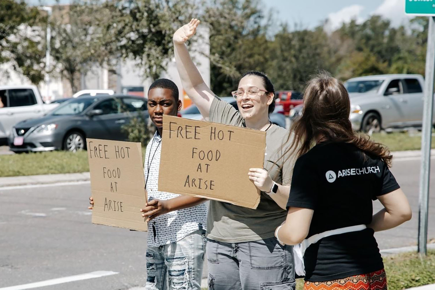 three people on the side of the road holding up free food signs