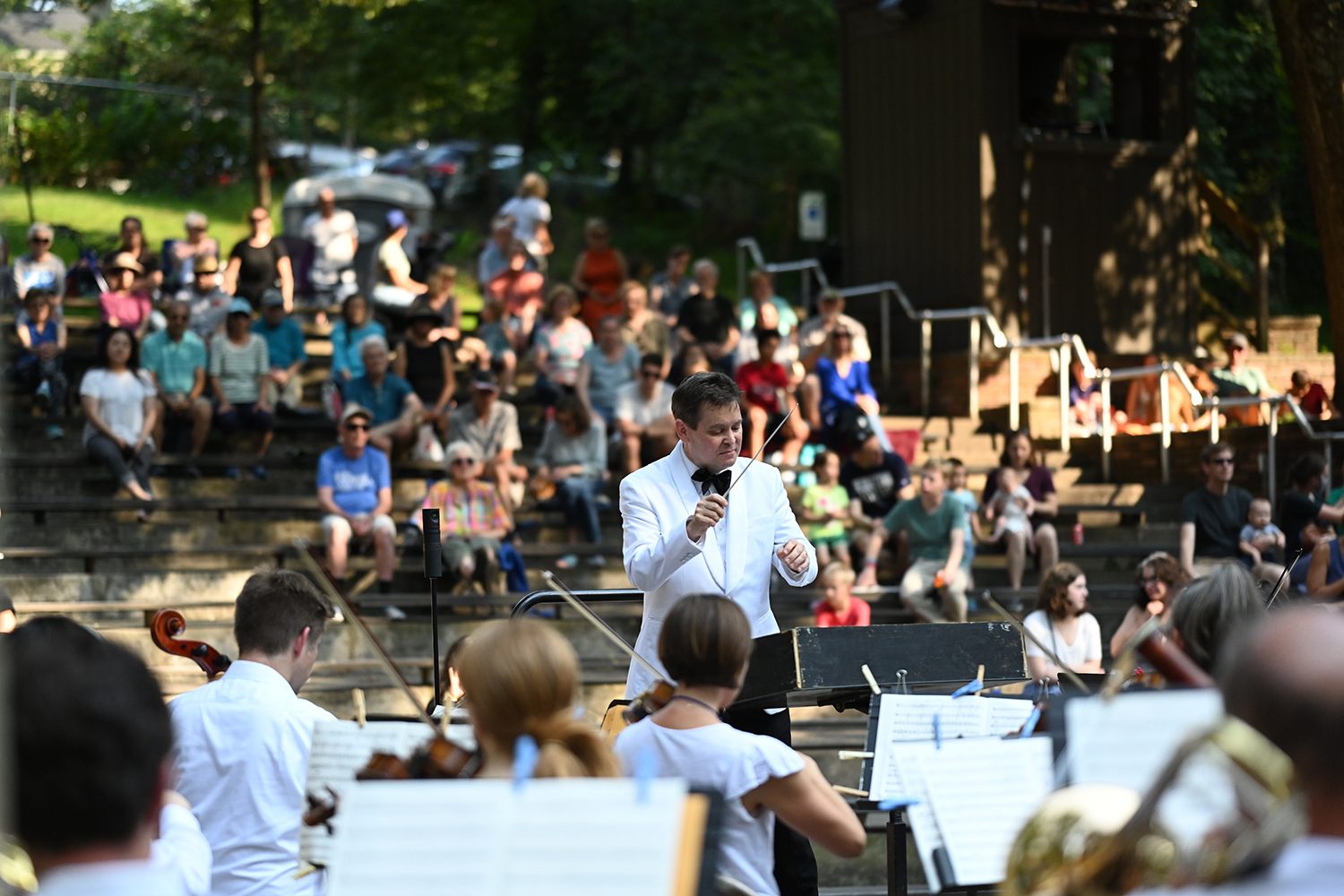 a conductor with an orchestra in an outdoor park setting