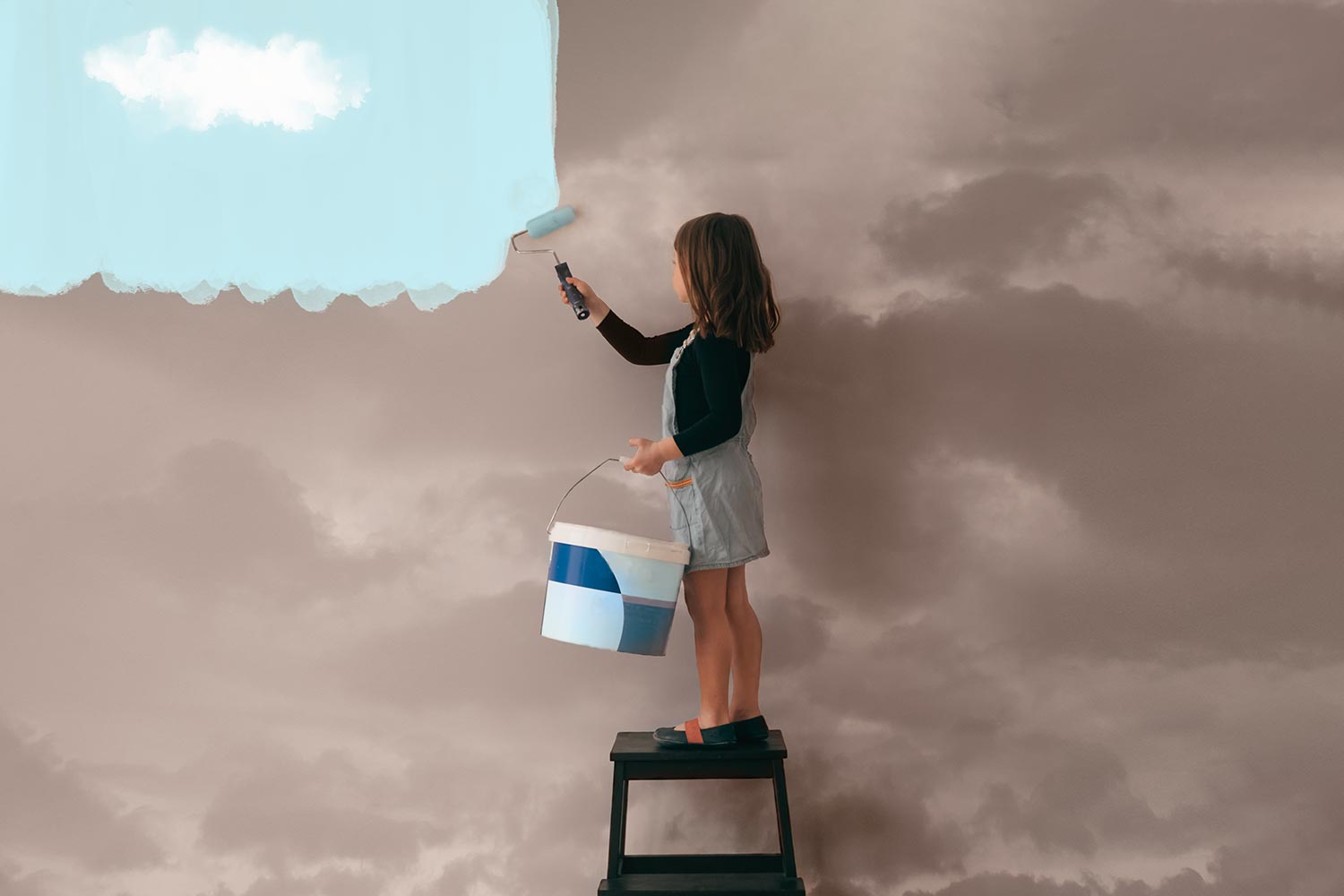 a girl on a stepladder painting a wall