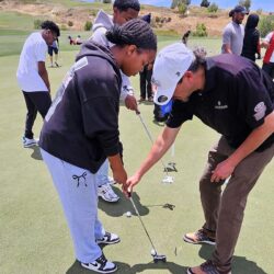 a man helps a girl hit a golf ball