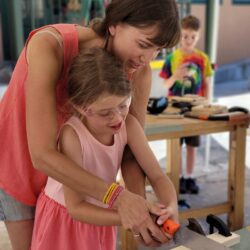 a woman helps a girl use a saw