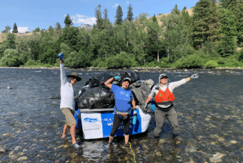 three people standing in a stream with bags of trash collected