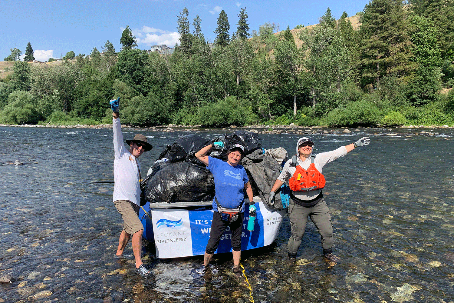 three people standing in a stream with bags of trash collected