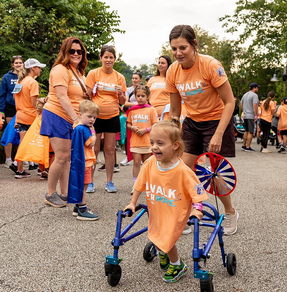 people outdoors helping a child walk with a walker