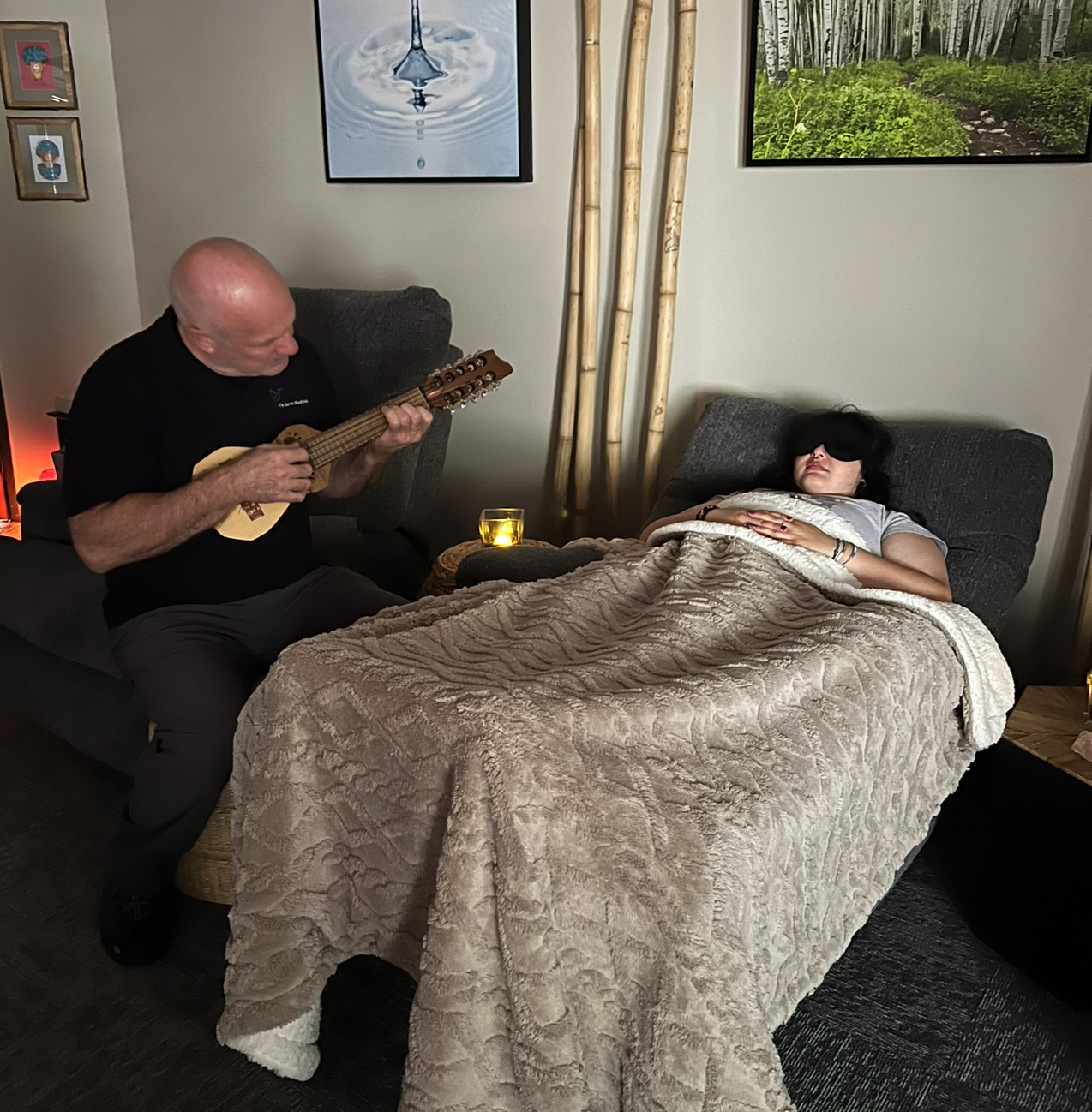 person playing a small guitar next to a young women resting in a bed
